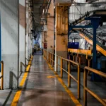 Tampilan luas interior pabrik modern dengan mesin industri dan sistem konveyor, menggambarkan proses manufaktur